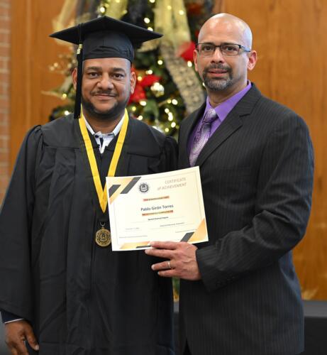 A graduate poses with his certificate while standing next to Miguel Figueroa.