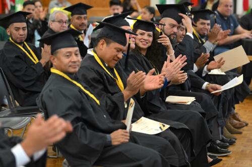 Graduates clap and smile while seated at the graduation.