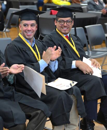 A close-up photo of two graduates smiling and clapping at the graduation.